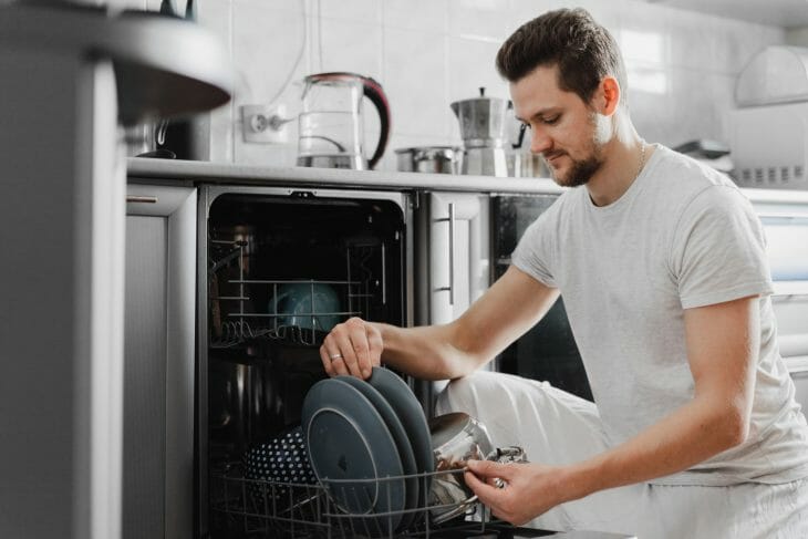 Мужчина достает посуду из посудомоечной машины